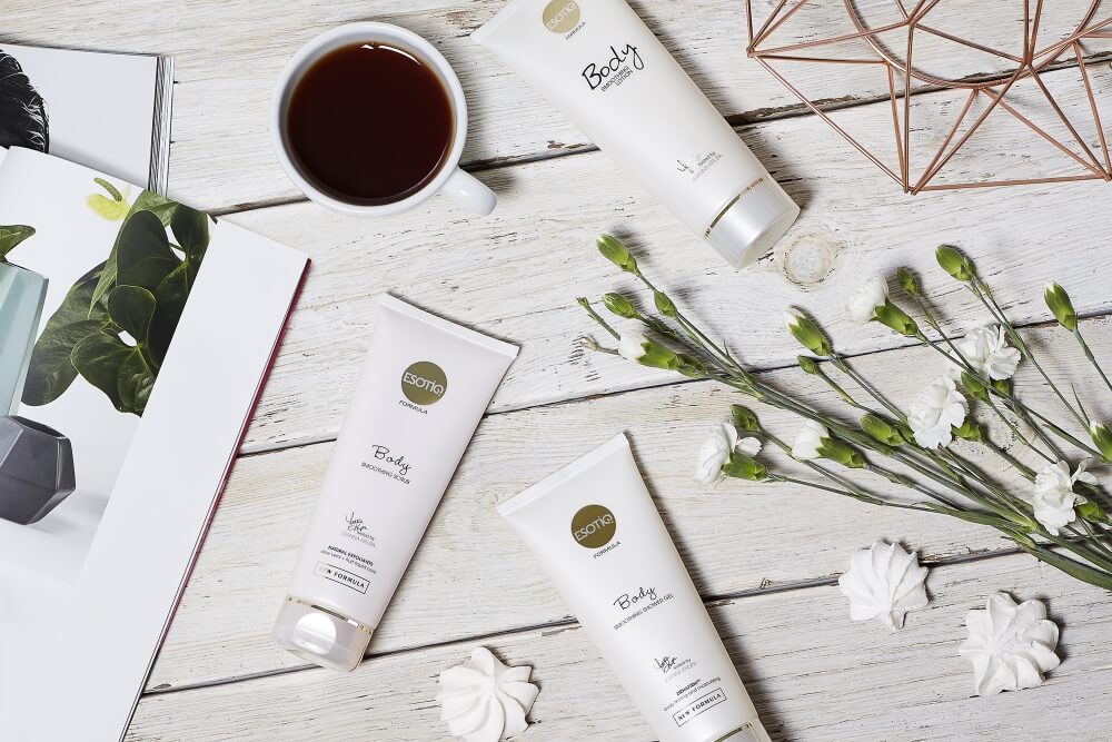 photo of body care Esotiq cosmetics on light wooden boards in arrangement with flowers coffee and a magazine