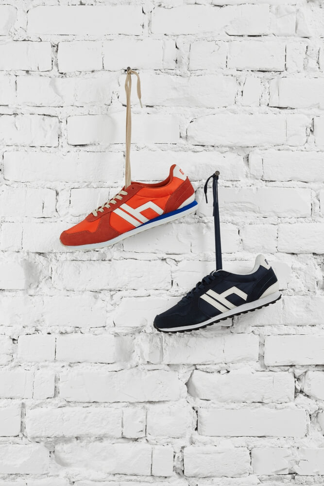 a still life photo of two pairs of shoes hanging on shoelaces ona brick wall painted white