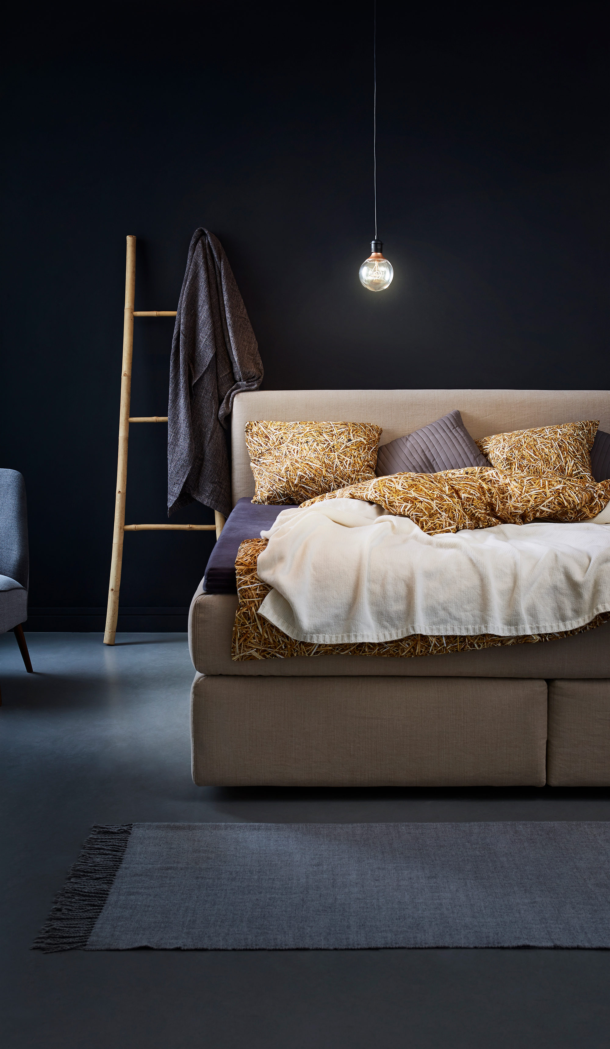 photo of a bed in a set of a room in grey navy blue colors with light source from a lamp above