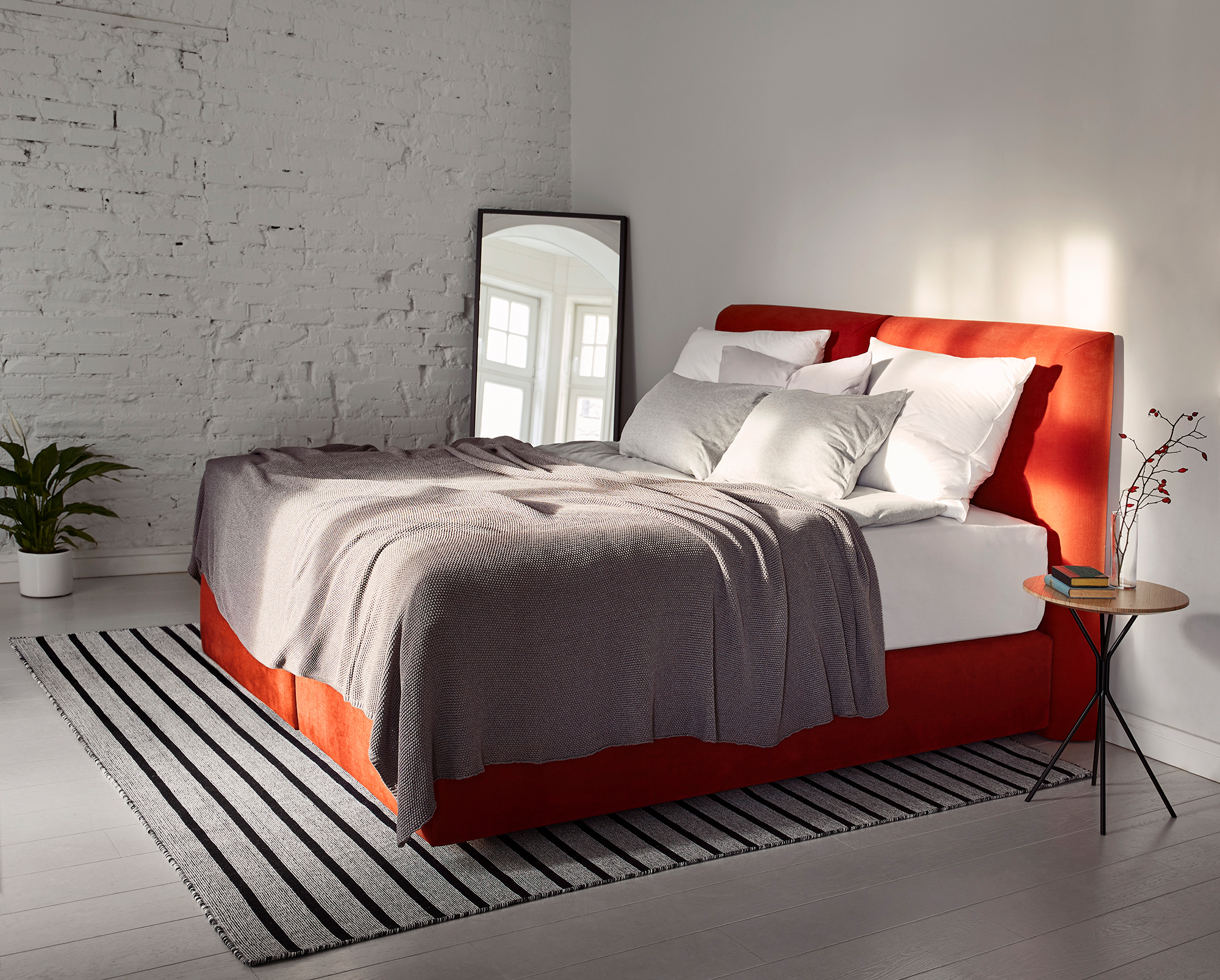 photo of a red bed in a set of s room with a painted white brick wall. photo with an effect of daylight coming from a window on the product