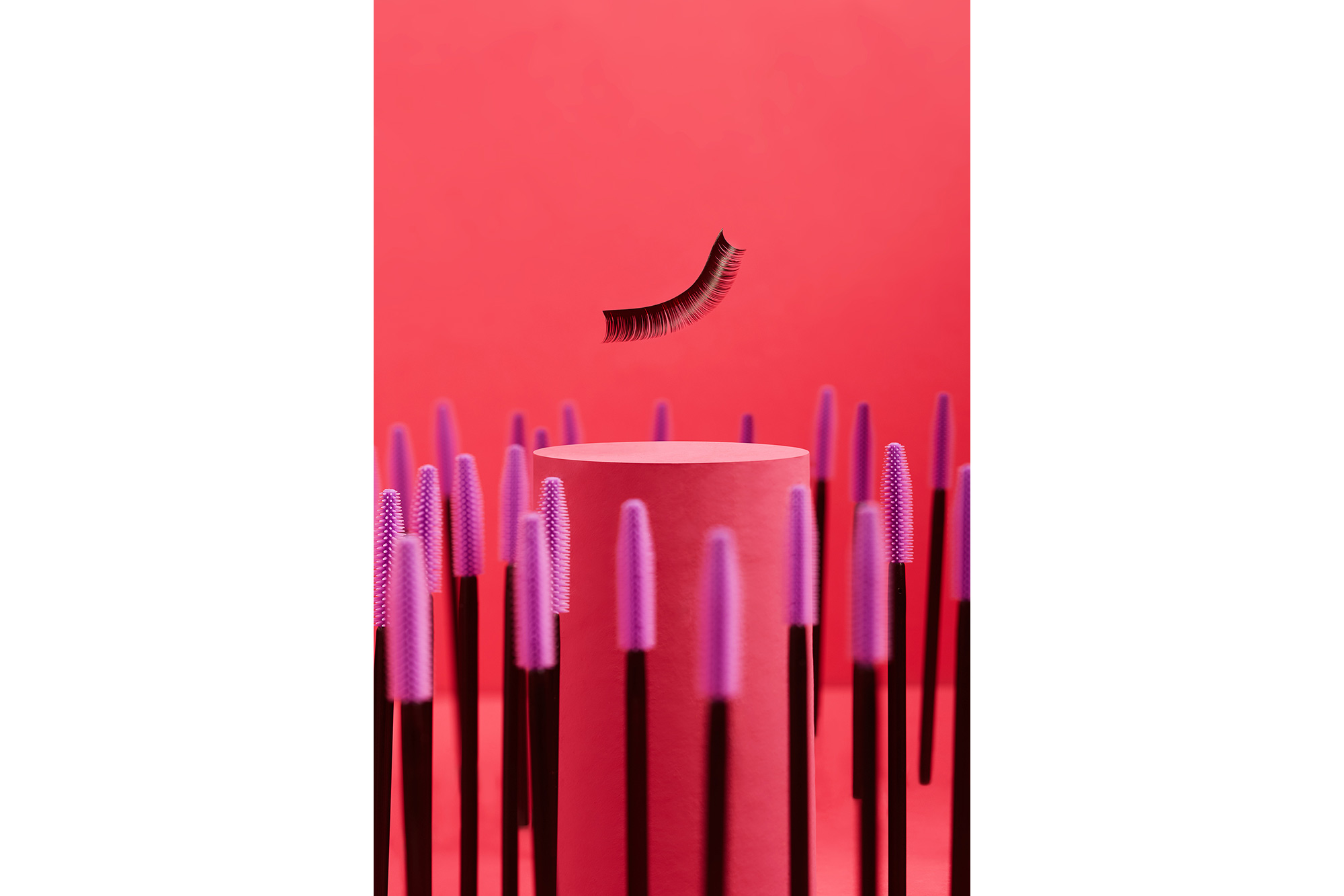 creative commercial photo of an lash hanging in the air above vertically placed lash brushes around cylindrical set decoration set in pink colour tone