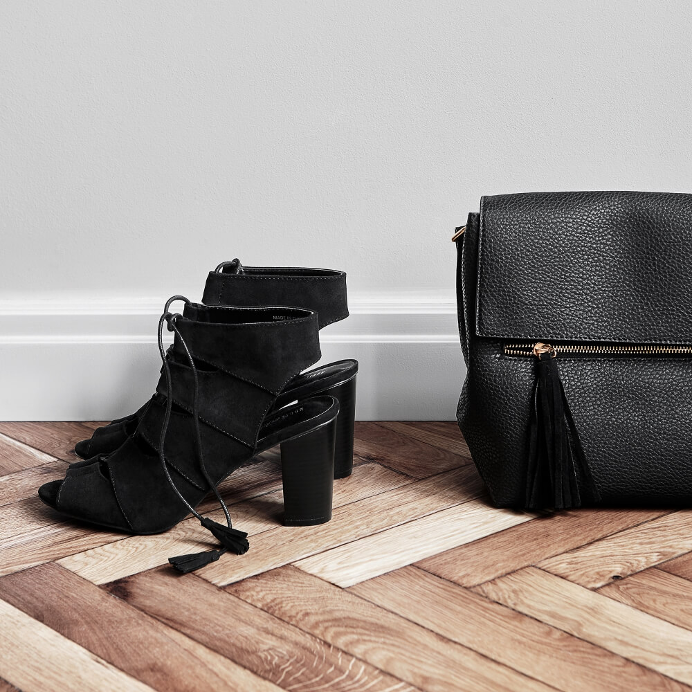 a photo of black shoes and purse on a white wall background standing on a parquet
